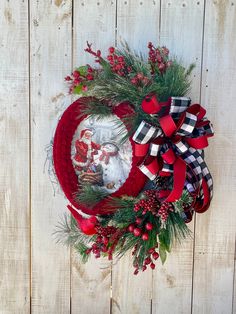 a wreath with red, black and white bows on it sitting against a wooden fence