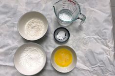 three bowls with eggs and flour next to a measuring cup on a white tablecloth