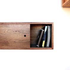 a wooden shelf with some pens and notebooks in it on top of a white wall