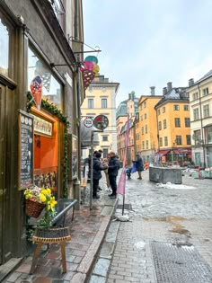 people are walking down the sidewalk in front of shops on a rainy day with umbrellas and flowers