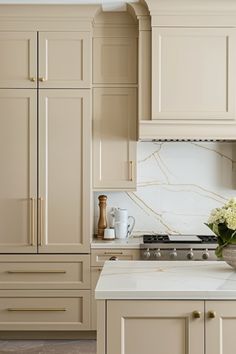 a kitchen with beige cabinets and white marble counter tops, along with a vase filled with flowers