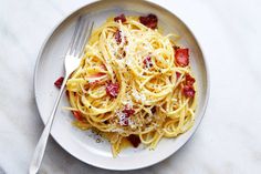 a plate of spaghetti with bacon and parmesan cheese on it, ready to be eaten