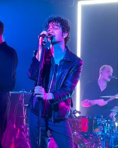 a man singing into a microphone while standing next to other men on stage in front of him