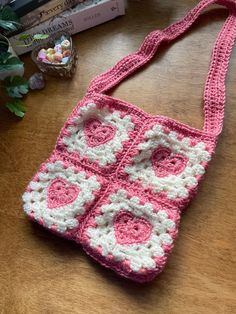 a pink and white crocheted bag sitting on top of a wooden table next to a plant