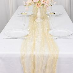 a white table topped with a vase filled with flowers and wine glasses on top of it