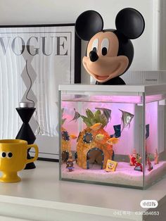 a mickey mouse figurine sitting on top of a table next to a fish tank