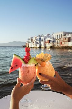 two people toasting with fruit on top of each other in front of the water