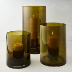 three green glass vases with one lit candle in the middle and two on each side