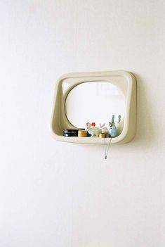 a mirror mounted to the side of a wall next to a shelf with various items on it