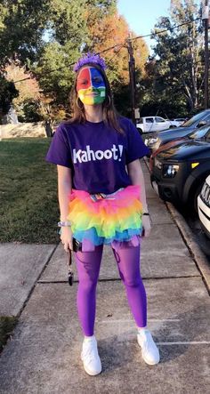 a woman in purple shirt and rainbow skirt standing on sidewalk