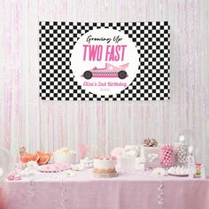 a pink and black checkered table cloth with two fast cars on it, surrounded by other desserts