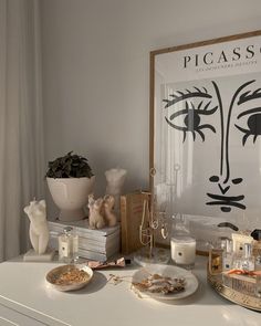 a white table topped with plates and candles next to a painting on the wall above it