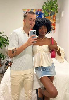 a man standing next to a woman holding a cell phone and taking a selfie