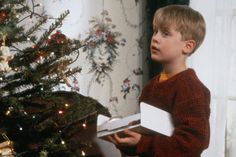 a young boy holding a present near a christmas tree