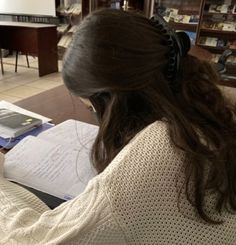 a woman sitting at a desk with papers in front of her, reading a book