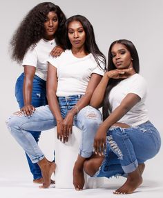 three women posing for a photo in jeans and t - shirts, with one leaning on the back of another woman's leg