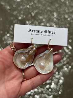 Capture the essence of the sea with these natural oyster shell earrings. Each pair is a unique testament to coastal beauty, showcasing the organic shapes of the ocean. Adorned with semi-precious pearls and delicately crafted with 14k gold and UV resin. Embrace the elegance of simplicity and let your accessories reflect the beauty of the natural world. Shells vary in size making sets 2-3 inches in height. *Each item is quality inspected before being sent out. Please be aware that items are handmade one at a time using multiple mediums throughout the creative process. Items may have minor imperfections. This is something we love about handmade items. Each small batch is unique and made with intention. Ocean-inspired Shell Pearl Earrings For Gift, Handmade Shell-shaped Pearl Earrings, Ocean-inspired Shell Pearl Earrings, Ocean-inspired Shell-shaped Earrings For Gifts, Ocean-inspired Shell-shaped Pearl Earrings, Natural Earrings, Oyster Pearl, Nature Earrings, The Creative Process