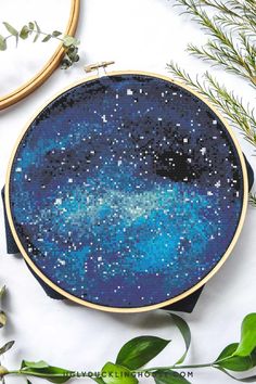 a cross stitch pattern with blue and white stars in the night sky, surrounded by greenery