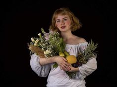 a woman holding a bunch of fruit and flowers