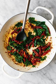 a skillet filled with spinach and sauce on top of a marble countertop