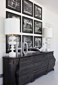 a black dresser sitting in front of a wall with pictures on it and two lamps