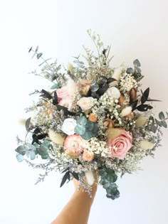 a hand holding a bouquet of flowers against a white background with greenery and leaves