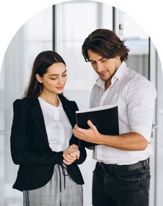 a man and woman standing next to each other in front of a glass wall holding an open book