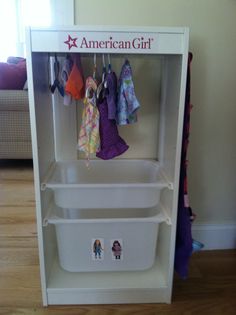 an american girl toy storage unit with clothes hanging on the hooks and two bins