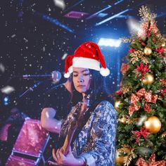 a woman in a santa hat playing the guitar next to a christmas tree