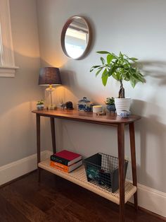 a wooden table topped with a potted plant next to a wall mounted mirror and lamp