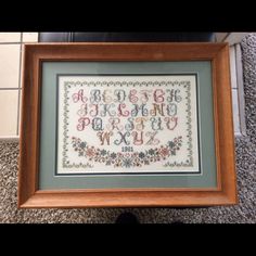 a cross stitch sample in a wooden frame on the floor next to a black cat