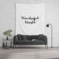 a white wall tapestry with the words wonderful world printed on it in black ink next to a gray couch