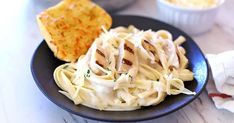 a black plate topped with pasta and meat next to other food on a white table