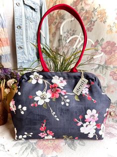 a blue floral purse with a red handle sitting on a table next to some plants