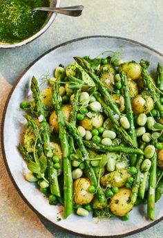 a white plate topped with asparagus and potatoes next to a bowl of pesto