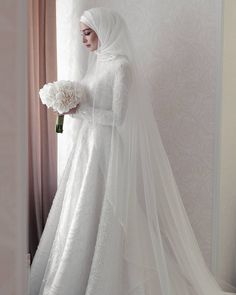 a woman in a white wedding dress holding a bouquet of flowers and wearing a veil