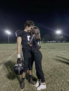 two football players embracing each other in the middle of a field at night with stadium lights behind them