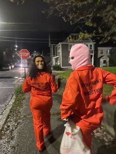 two people in orange jumpsuits walking down the street at night with one person wearing a mask