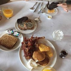 three plates with breakfast foods on them are sitting on a white tablecloth, and there is a glass of orange juice in front of the plate