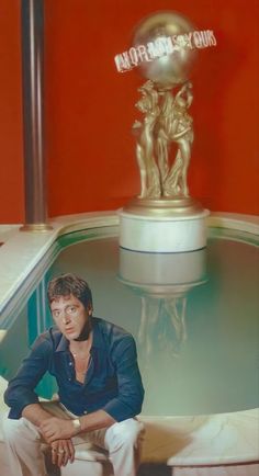 a man sitting in front of a fountain next to a golden trophy on top of a table