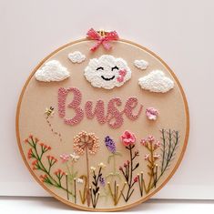 an embroidered wall hanging with the word base surrounded by flowers and clouds in pink, red, white and yellow colors