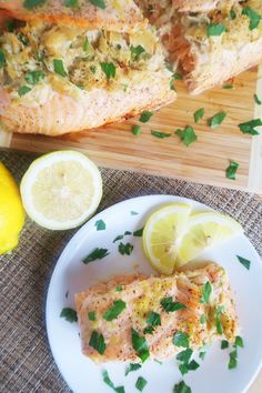 a white plate topped with fish next to lemon wedges and a slice of lemon