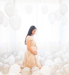 a pregnant woman standing in front of white balloons with her belly tucked under her stomach