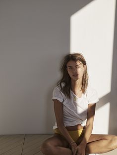 a woman sitting on the floor in front of a white wall with her legs crossed