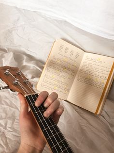 a person is holding an ukulele in their hand and reading it on the bed