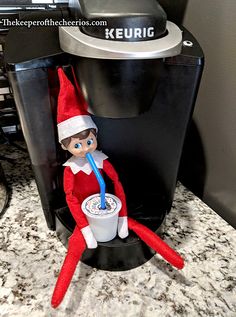 an elf is sitting on top of a coffee maker with a drink in his hand