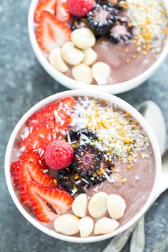 two bowls filled with fruit and nuts on top of a gray table next to spoons