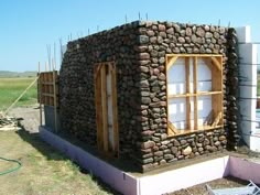 a building made out of rocks and wood with windows on the side, surrounded by construction materials