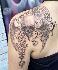 a woman with a skull and angel wings tattoo on her back, showing the upper half of her shoulder