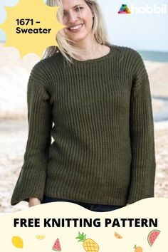 a woman standing in front of the ocean wearing a green sweater and jeans with her hands in her pockets